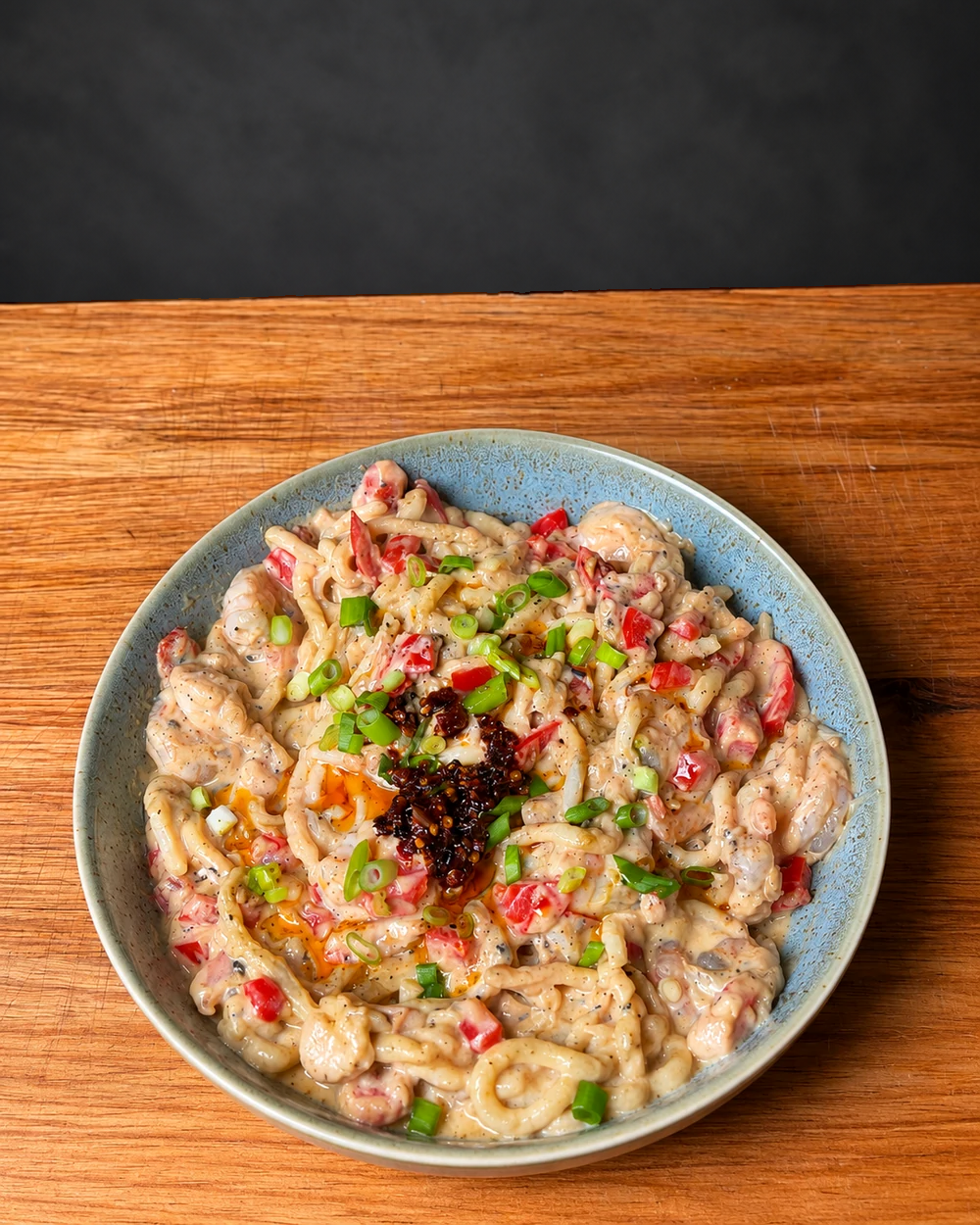 Bowl of udon in a creamy sauce with prawns, capsicum and chilli crisp