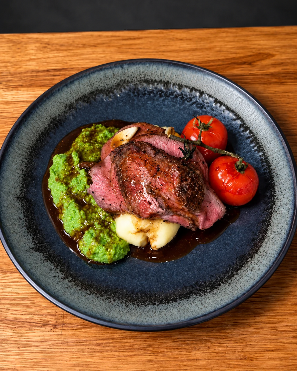 Sliced pink lamb leg with pea puree, mash and roasted vine tomatoes